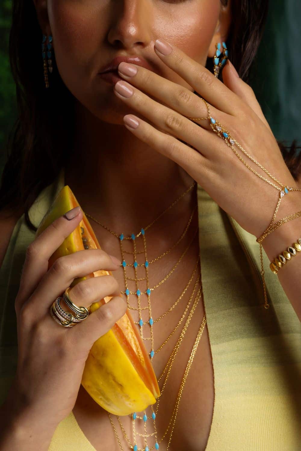 Woman wearing gold necklaces and bracelets, holding a yellow fruit.