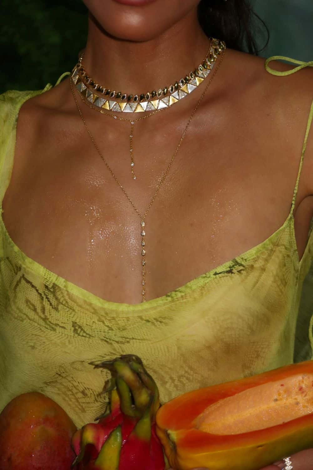 Woman wearing a yellow top with a necklace, holding a papaya and other fruits.